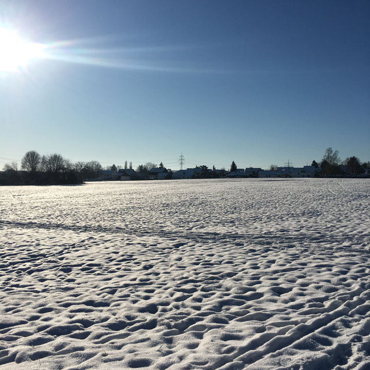 Verschneite Wiese und Dorfsilouette in strahlendem Sonnenschein