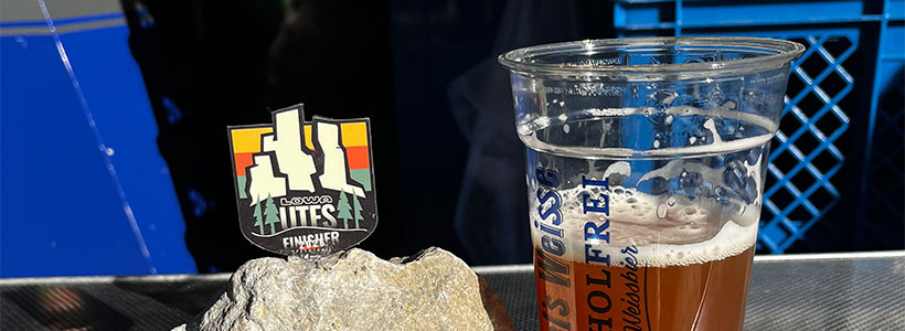 Ein Brocken fränkischer Kalkstein, in den eine kleine Medaille "LOWA UTFS Finisher Speedtrail" eingearbeitet ist. Daneben ein halb leerer Plastikbecher mit alkoholfreiem Weizen.